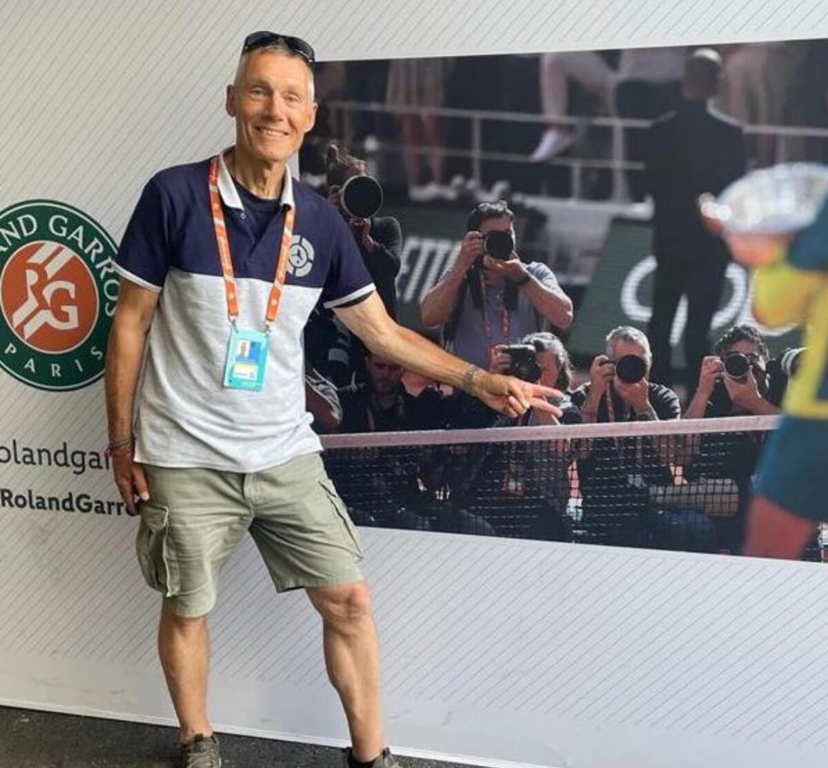 Hasenkopf poses in front of a photograph at the French Open.  In the image, he is in the front row with other photographers, photographing the awards ceremony after the final.